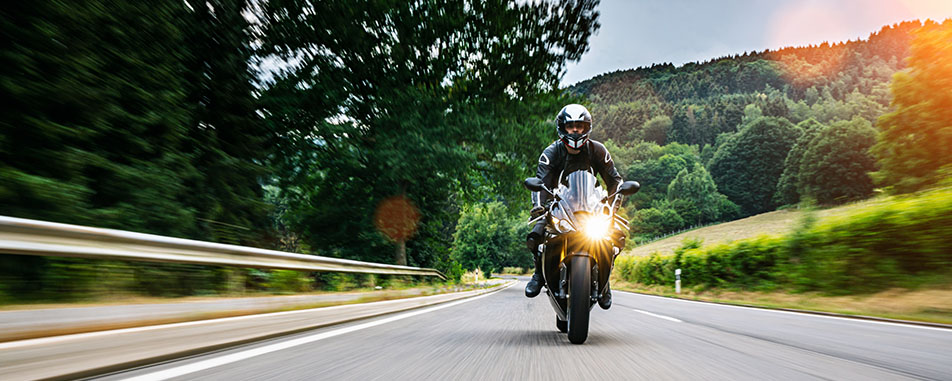 Motorcyclist riding a black sport bike at speed on a winding country road - https://www.fairwayinsuranceadvisors.com/