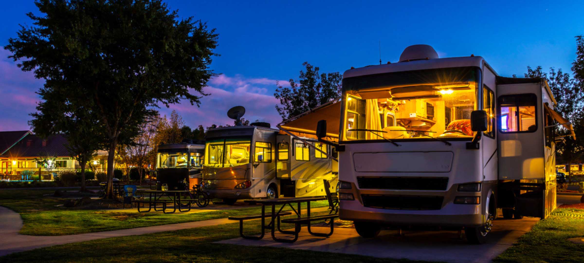 RV campground at dusk with lit motorhomes - https://www.fairwayinsuranceadvisors.com/