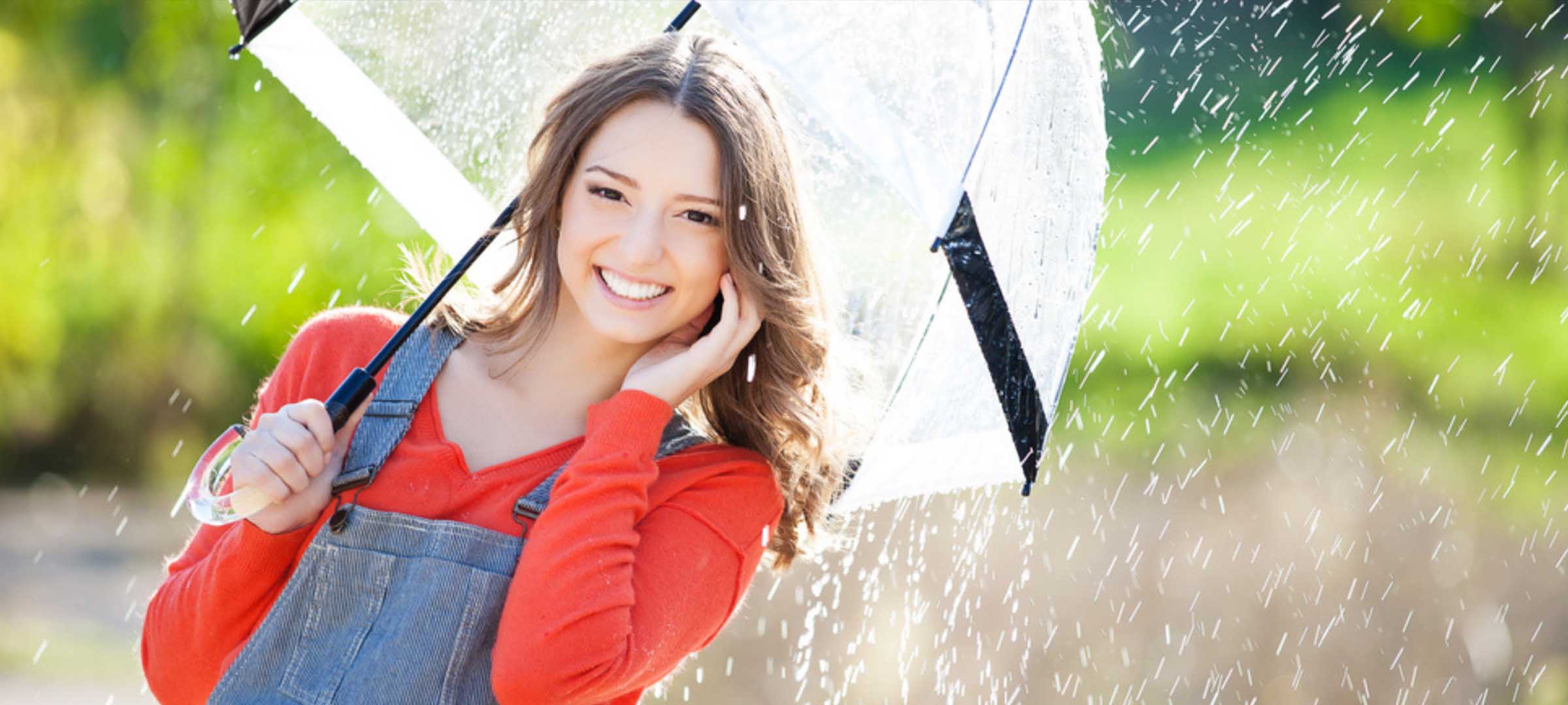 Young person in red long-sleeve shirt and denim overalls holding a clear umbrella - https://www.fairwayinsuranceadvisors.com/